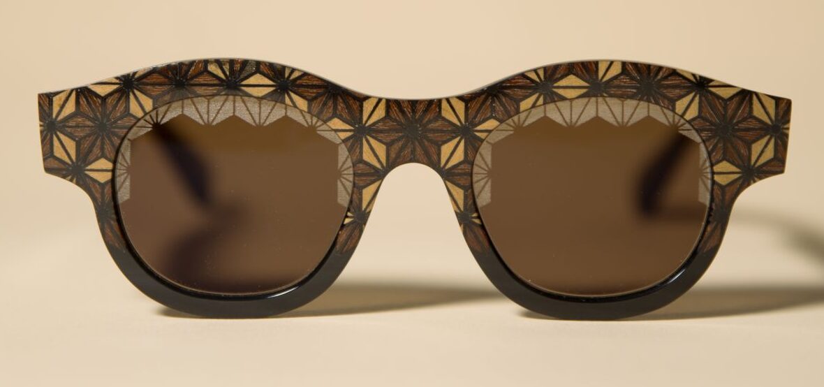 Brown sunglasses with a geometric, starburst-pattern frame and dark lenses on a beige background.