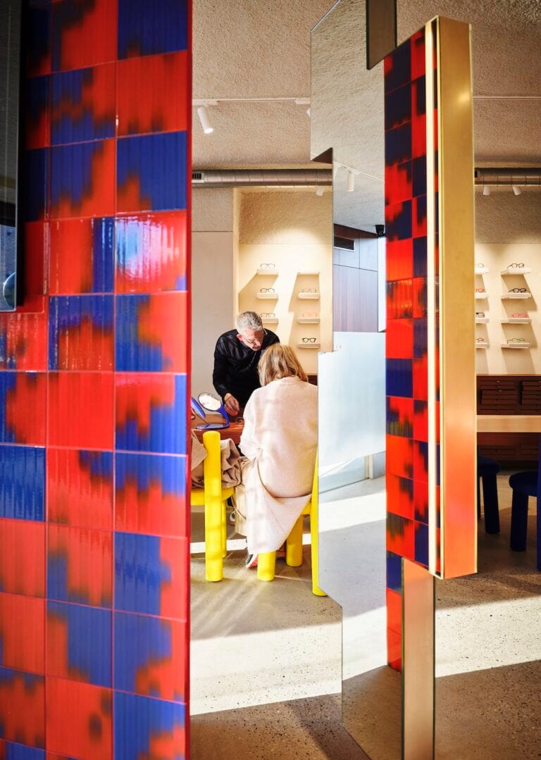 © 2026 Alain Six for ID6o10 | Eyestylist Two People Sit at a Counter Inside a Colorful Eyewear Shop, Shelves of Frames Visible in the Background. | Eyestylist 21st May 2026