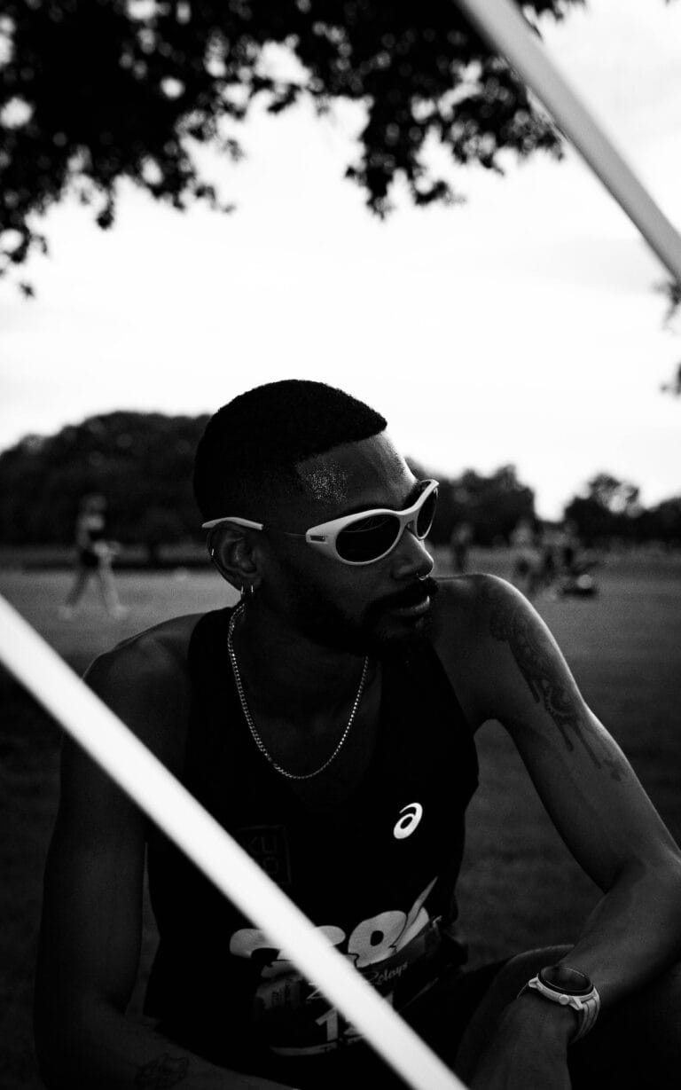 Black-and-white Photo of a Man with Short Hair Wearing White Sunglasses and a Sleeveless Shirt, Sitting Outdoors in a Park.  | Eyestylist 2nd May 2026