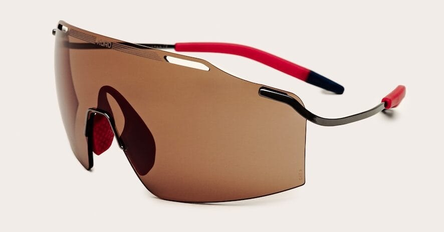 Wraparound single-lens sunglasses with brown tint and red/black temples, product shot.