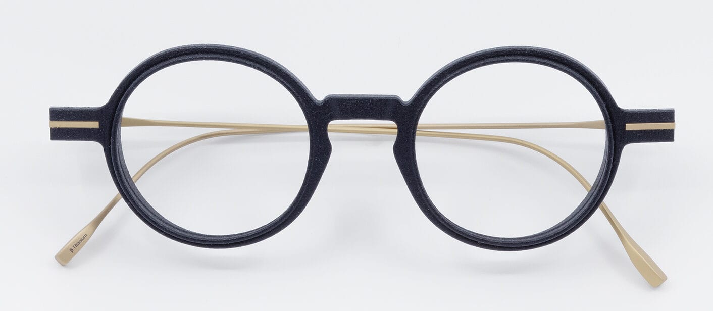 Round black eyeglasses with beige temples resting on a white surface.