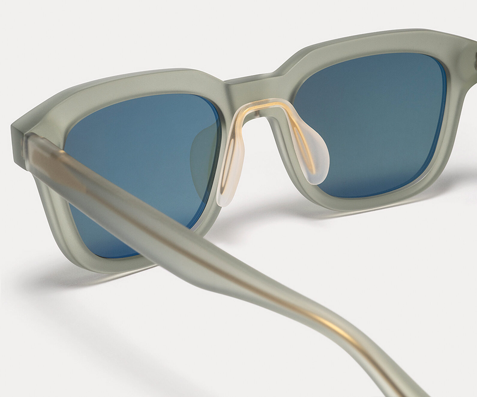 Close-up of oversized sunglasses with blue lenses and light gray frames, showing curved temples.