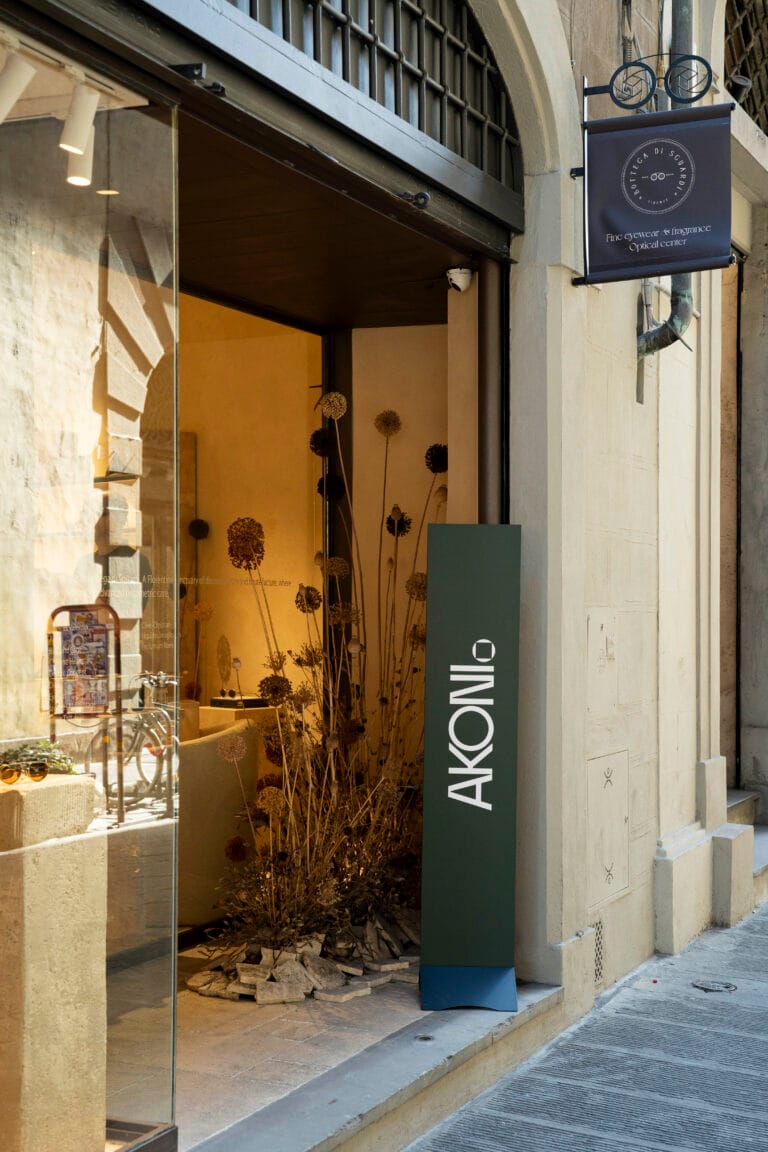 Akoni_Firenze_rush 9 | Eyestylist Exterior Shopfront with a Dark Green Vertical Sign Bearing White Letters Next to a Glass Display Window and Dried Flower Decor Inside. | Eyestylist 19th June 2026