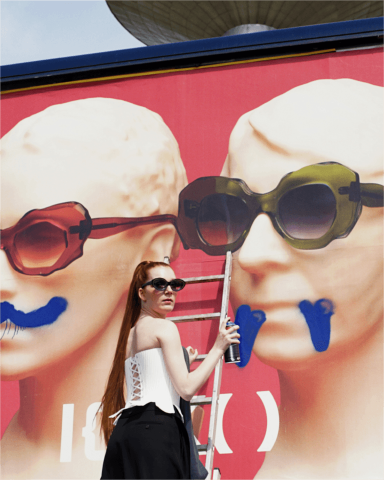 IOKO-Studio-AMY-Social-Portraits-v01_07-01 | Eyestylist Woman on a Ladder Painting a Giant Mural of Two Faces Wearing Sunglasses on a Pink Wall. | Eyestylist 15th June 2026