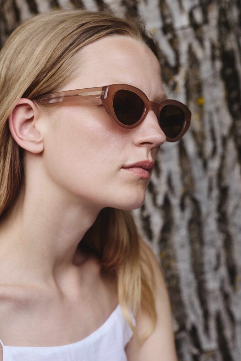 22_Pomandere_755_HQ | Eyestylist Close-up of a Woman Wearing Brown Round Sunglasses, with Blonde Hair, Against a Textured Tree Trunk Backdrop. | Eyestylist 14th July 2026