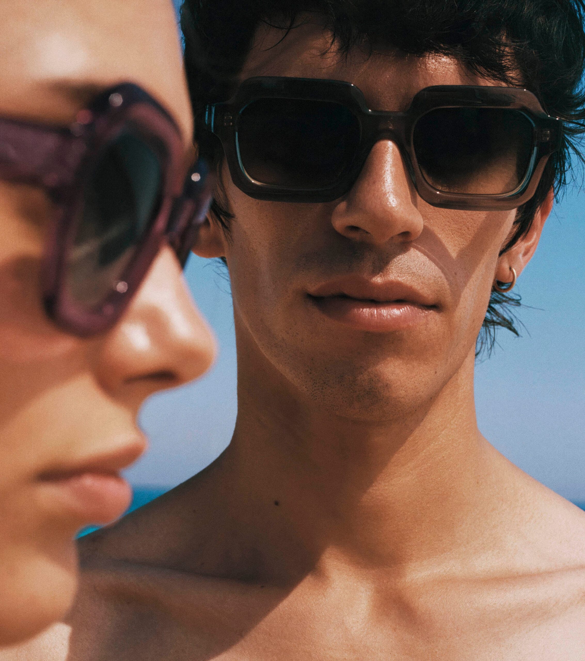 Two people wearing dark sunglasses, close-up outdoors with a blue sky background (sunny day).