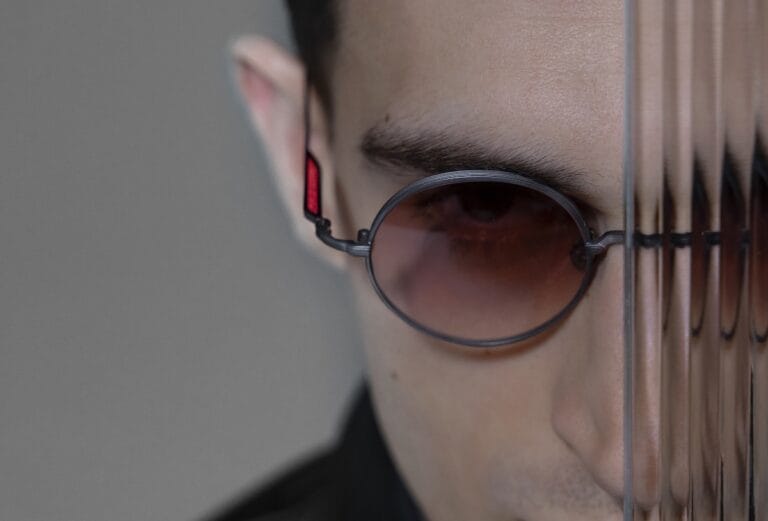 M3168SGMBK1 | Eyestylist Close-up of a Person Wearing Round Metal Sunglasses with Red Lenses, Partially Obscured by Vertical Blinds. | Eyestylist 10th July 2026