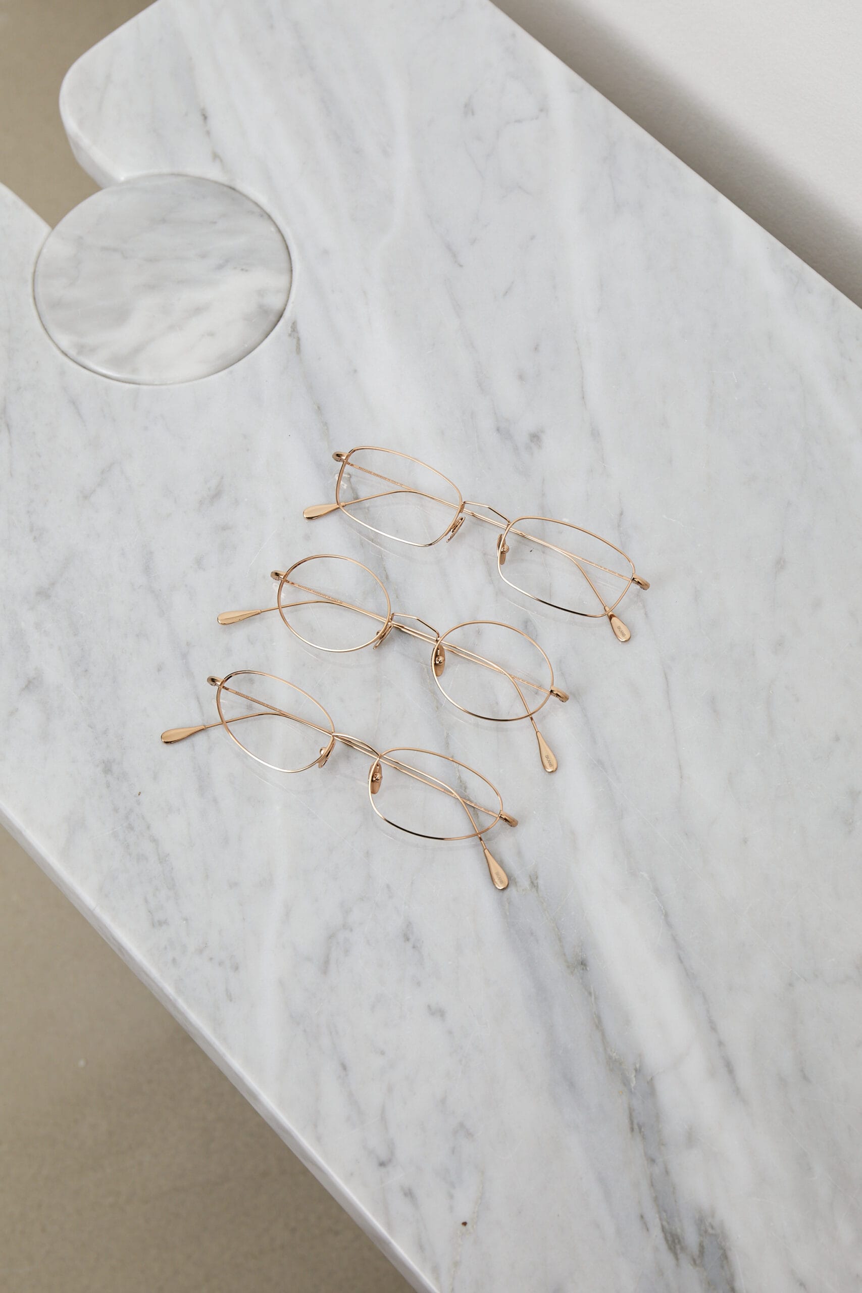 Gold wire-frame eyeglasses with round lenses resting on a white marble table.