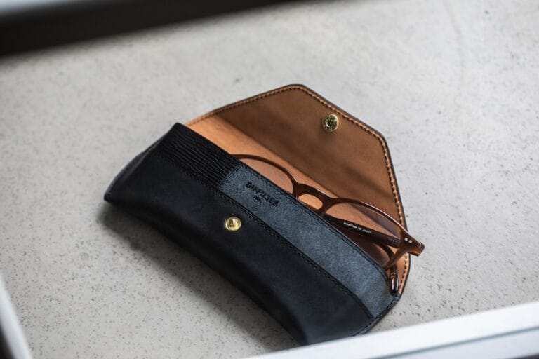 Open Black and Tan Leather Eyeglasses Case with Brown-framed Glasses Inside on a Light Speckled Surface.  | Eyestylist 5th August 2026