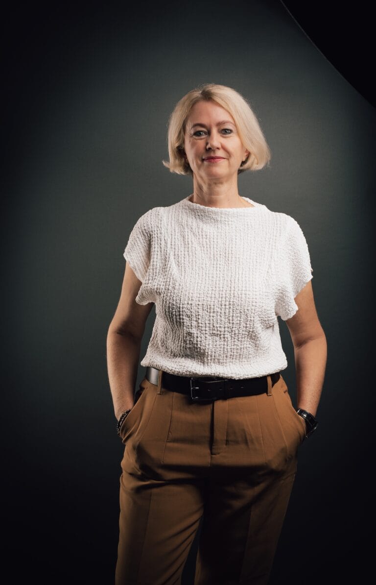 Woman with Short Blonde Hair Wearing a White Textured Top and Brown Trousers, Hands in Pockets, Studio Backdrop.  | Eyestylist 15th September 2026