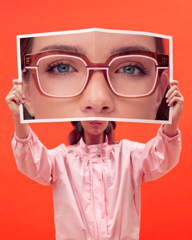 FACEAFACE_SOUL2_COL_3063 | Eyestylist Child Holds a Large Photo Frame with Oversized Pink Glasses in Front of Her Face Against an Orange Background. | Eyestylist 1st September 2026