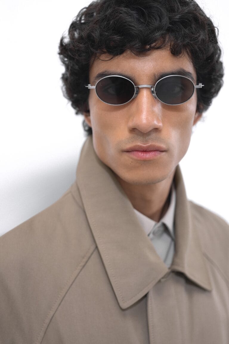 KALEOS-FW26-MAN-21 | Eyestylist Close-up of a Person Wearing Round Black Sunglasses and a Beige Trench Coat, Facing the Camera. | Eyestylist 14th September 2026