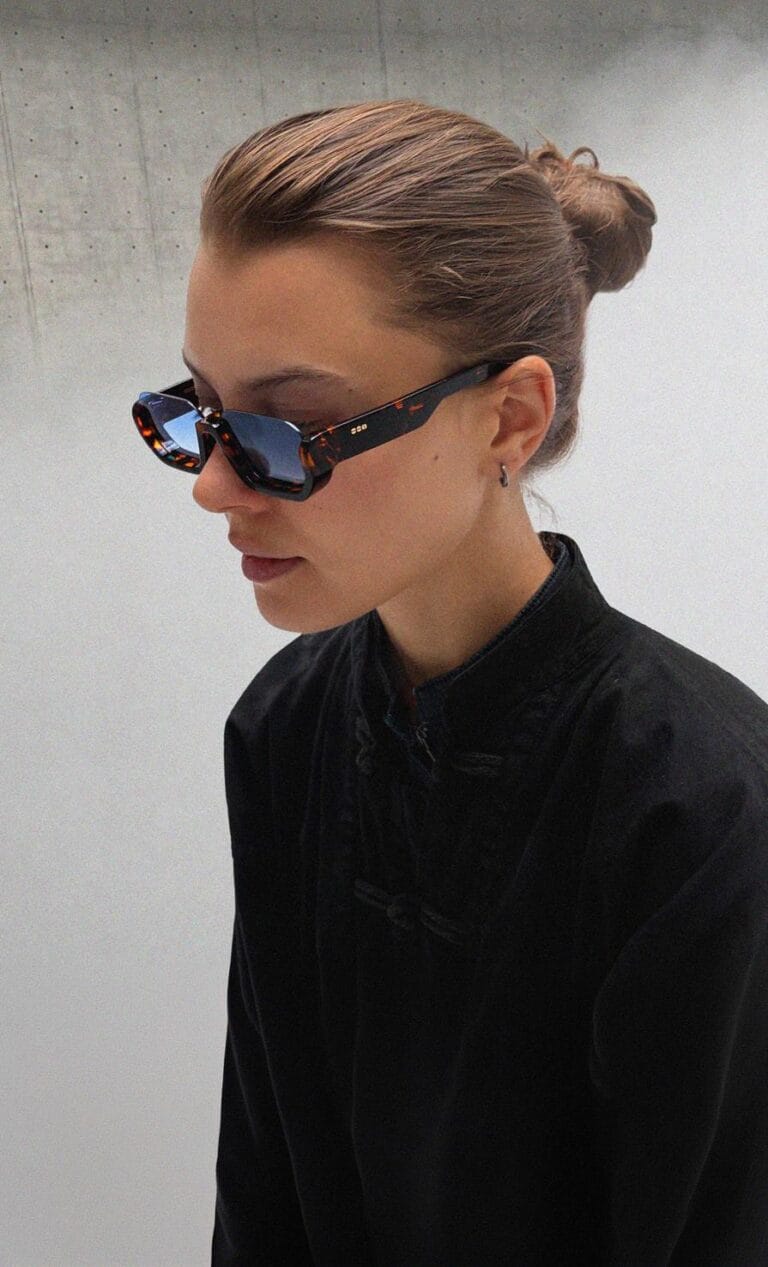 mainimagebigger_LR-9906db0b6d04513c | Eyestylist Profile View of a Person Wearing Dark Tortoiseshell Sunglasses and a Black Mandarin-collar Jacket, Hair in a Bun, Looking Downward. | Eyestylist 9th September 2026